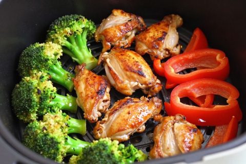 Air fryer basket with cooked chicken and roasted vegetables.
